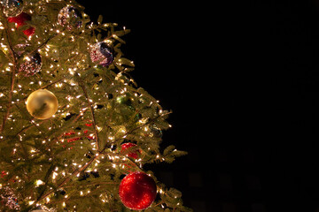 Christmas tree with colourful decorations and lights against black background
