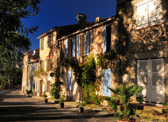 Fototapeta na wymiar Trees Giving Shade To Sun Lit Mediterranean House Facades In Gassin Provence France On A Beautiful Autumn Day With A Clear Blue Sky