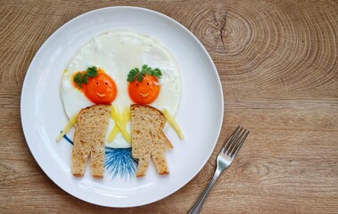 
Boy and girl fried egg made it from egg,wholewheat bread,cheeses,black sesame and parleys on plate with wooden table background.Art food idea for kids breakfast.Top view.Copy space