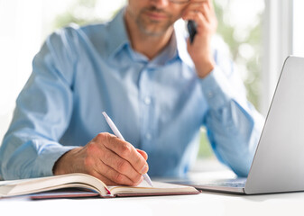 Mature businessman writing in diary at desk in office