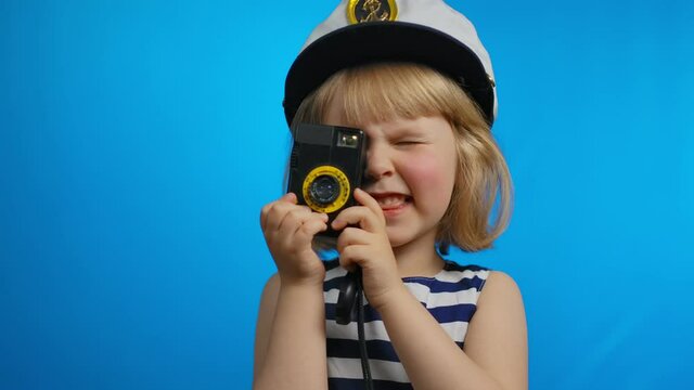 Cute girl in a sailor dress is using a retro photo camera for shooting pictures