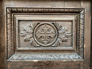 Engraved cross symbol with ornaments on old wooden door of a christian church.