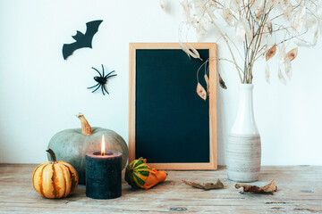Halloween composition with blackboard, pumpkins, candle and dried flowers in vase, bat and spider....
