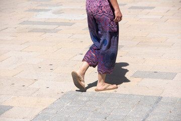 Close-up of a woman's legs with casual pants, and with sandals while walking down a street in Mexico in the summertime