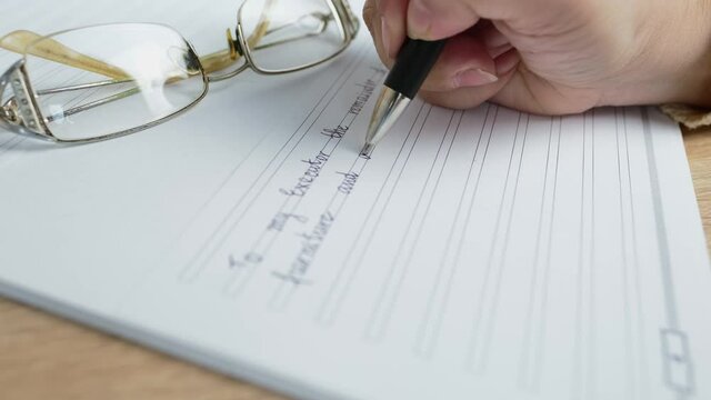 close-up female hand writes with a pen on paper the words of will, the concept of a legal order on her movable and immovable property in the event of a person's death for the heirs