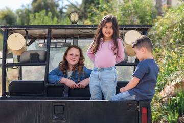Smiling children having fun in the back of their pickup truck enjoying the road trip in country side. Little kids in pickup truck on camping trip. - obrazy, fototapety, plakaty