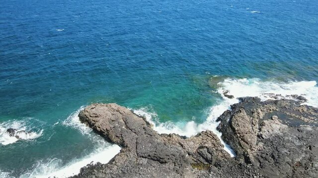 Drone view of a volcanic shore and the clear, blue Atlantic Ocean with breaking waves and underwater rocks. Down tiliting, high angle aerial shot.