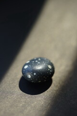 Black pebble stone with white spots on it at black sunny table