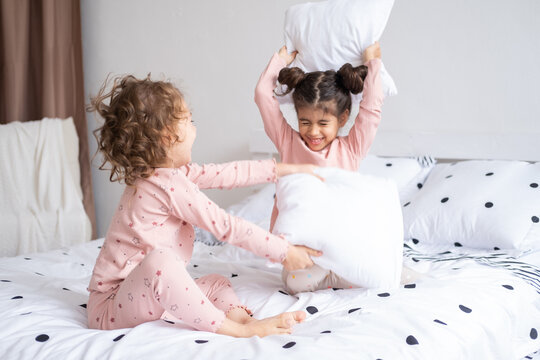 two kids girls in pajamas having pillow fight on bed in modern bright apartment