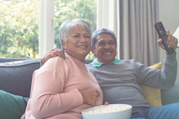 Two diverse senior couple sitting on sofa, watching tv and having fun