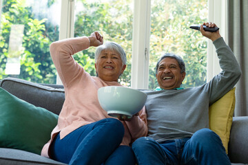 Two diverse senior couple sitting on sofa, watching tv and having fun