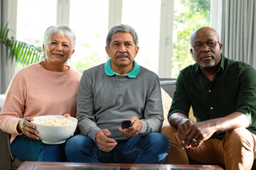 Two focused diverse senior couple and their african american male friend watching tv and having fun