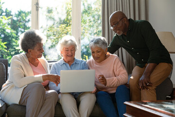 Three happy diverse senior woman and african american male friend sitting on sofa and using laptop