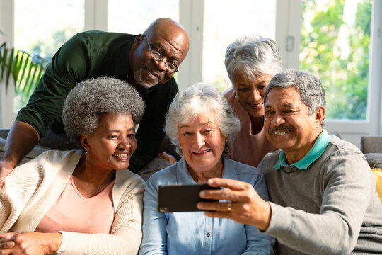 Five happy diverse senior friends sitting on sofa and looking at smartphone