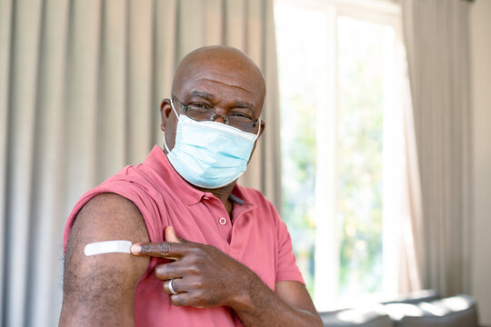 Senior african american man in face mask showing plaster after vaccination
