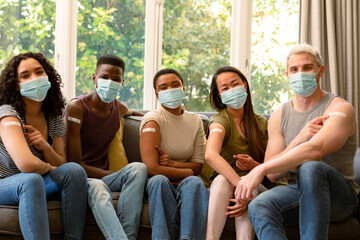 Group of happy diverse female and male friends in face masks showing plasters after vaccination