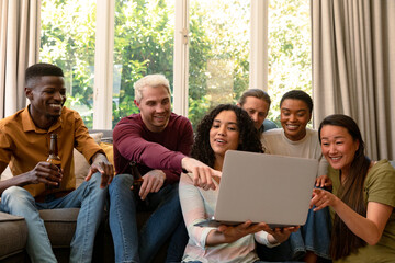 Group of happy diverse female and male friends drinking beer together and using laptop