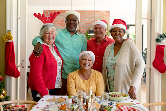 Diverse group of happy senior friends in holiday hats celebrating christmas together, taking photo