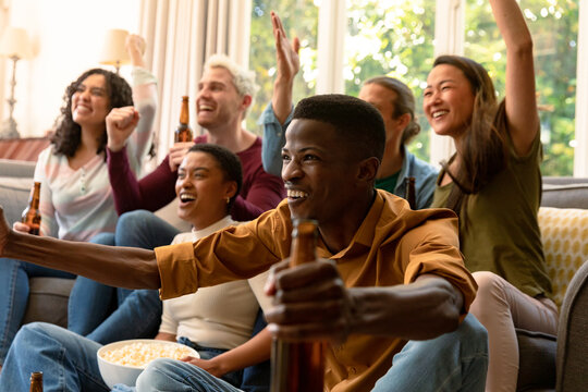 Group Of Happy Diverse Female And Male Friends Watching Tv And Drinking Beer Together At Home