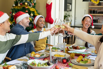 Group of happy diverse female and male friends toasting, celebrating christmas at home