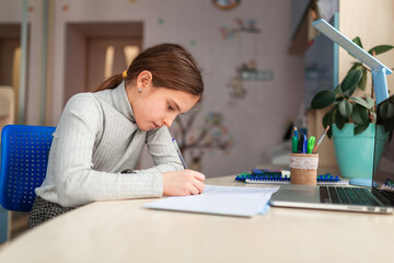 Naklejka premium Cute little schoolgirl studying at home doing school homework. Distance learning online education