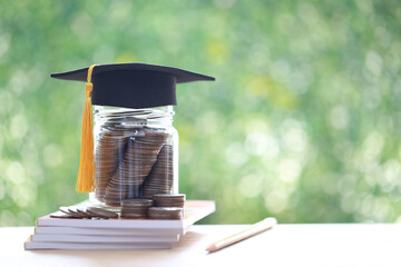 Graduation hat on coins money in the glass bottle on natural green background, Saving money for...