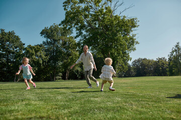 Active father with two little children, boy and girl playing together in green park on a summer day. Happy family enjoying leisure activity