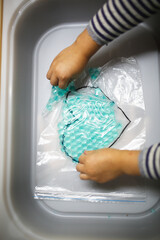 A child plays in the Sensory hydrogel box, children's hands touch, roll and play with blue water beads in a zip bag, Sensory development and Montessori, themed activities with children © natalialeb