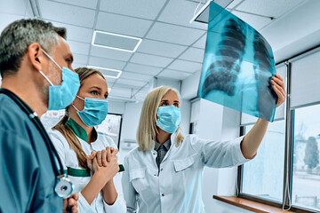 Doctors looking to and discussing x-ray image at hospital. Radiology, surgery, people and medicine concept.