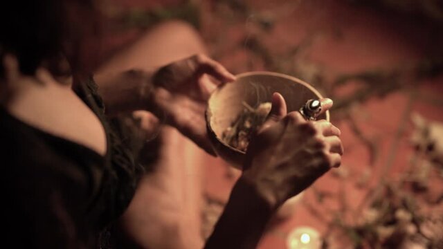 Crop witch conjuring over bowl with herbs