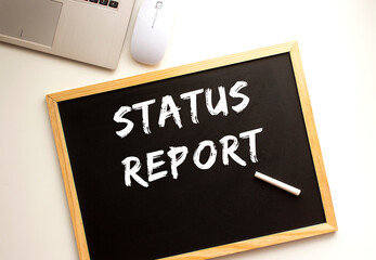 Text STATUS REPORT written in chalk on a slate board. Office desk.