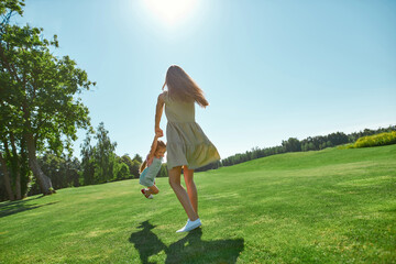 Full length shot of mom and little daughter spending time together on grass field in summer park
