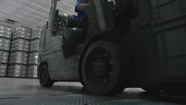 Forklift with Heavy Load Drives onto Ramp Past Camera In Manufacturing Warehouse