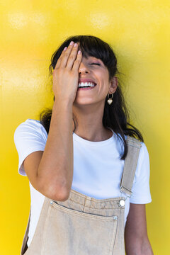 Woman with eyes closed covering eye in front of yellow wall