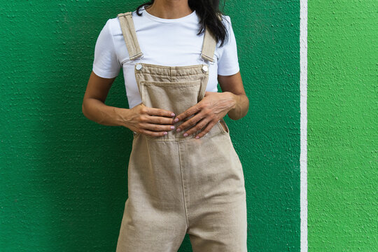 Woman wearing bib overalls in front of green wall