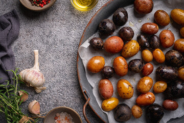 Various varieties of baked new colorful, white, red and purple potatoes on gray background, top view