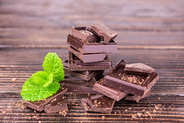 Bitter dark chocolate pieces with green mint on a dark wooden background.