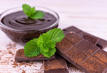 Pieces of dark chocolate and chocolate in a plate, sprinkled with cocoa on a white wooden background.	