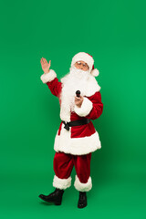 Santa claus in costume holding microphone and pointing at green background