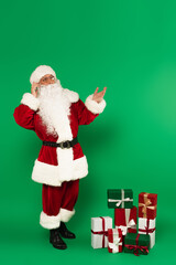 Santa claus talking on smartphone near presents on green background