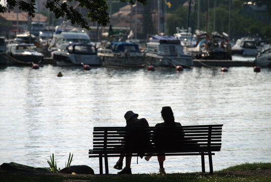 Silhouette of a couple of young people on a bench on the background of a yacht pier. Selective focus.