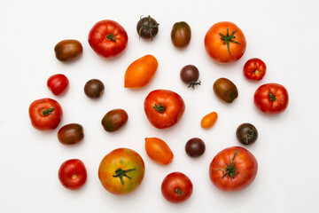A pattern of large and small tomatoes of various colors and shapes on a white background. Flat lay
