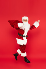 Santa claus with sack pointing with hand and levitating isolated on red
