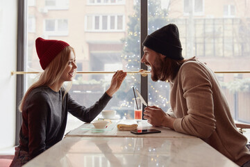 Blonde girl feeding her bearded boyfriend in cafe