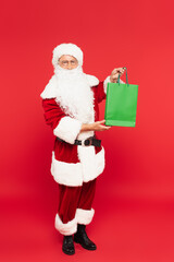 Santa claus in costume holding shopping bag on red background