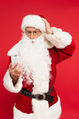 Worried santa claus using smartphone isolated on red