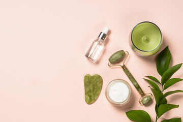 Jade roller and gua sha massager with serum bottle and cream at pastel background. Anti-aging therapy. Top view with copy space.