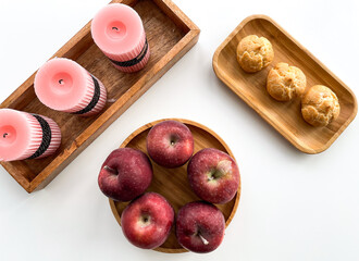 White table decorated with pink candles. Wooden plate with ripe red apples and fresh pastries. Wooden decoration on the kitchen table. Cozy home table setting