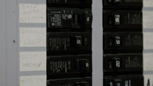 Male electrician turning off power for electrical outlet at circuit breaker box. Resetting Tripped breaker 