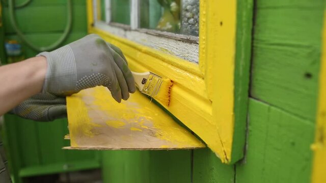 Paints the house. Paints a wooden house with a brush. Green and yellow paints
